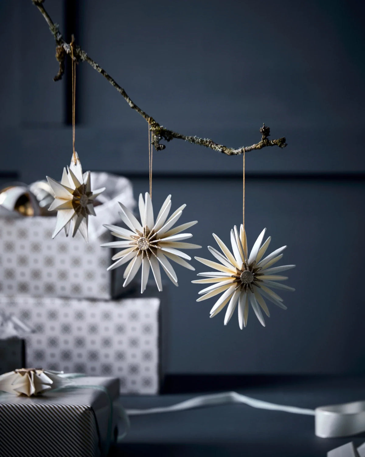 Decorative star-shaped HDStar ornaments by House Doctor, Champagne colour, hanging from a branch against a dark background.