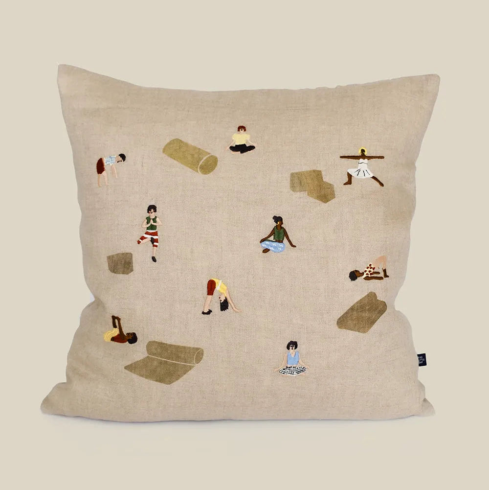 Decorative pillow with embroidered illustrations of people doing yoga poses and yoga gear on a natural linen background