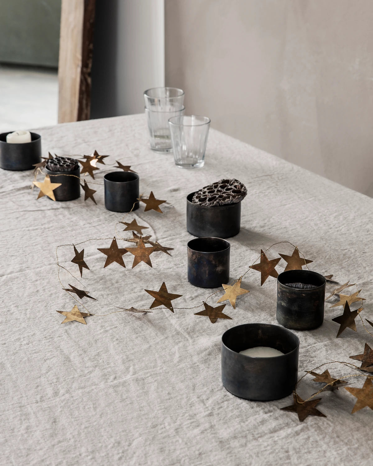 House Doctor antique brass star garland ling across a linen table cloth with black brass candle holders in between