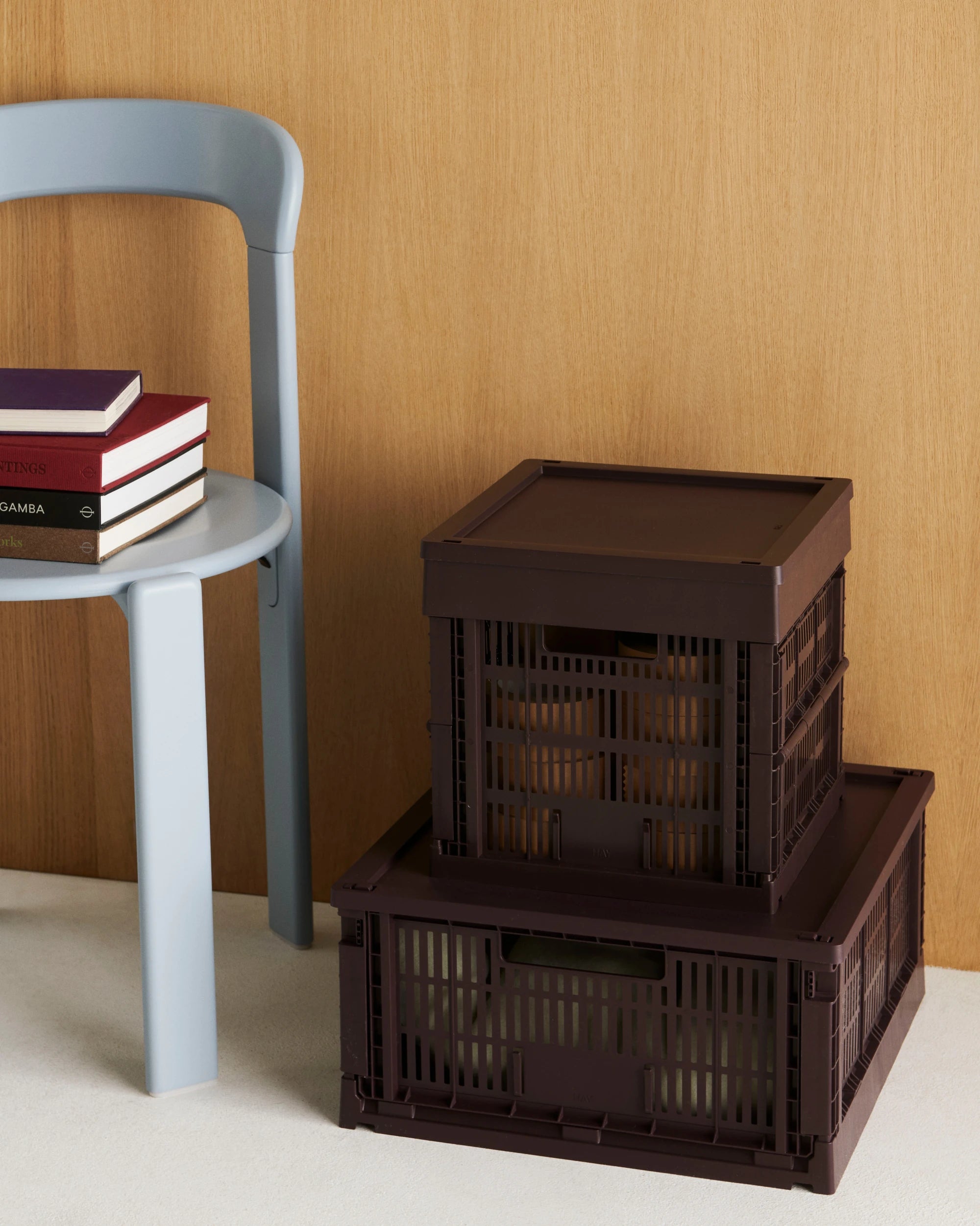Two HAY Square Colour crates stacked on a light surface with a gray chair and books in the background.