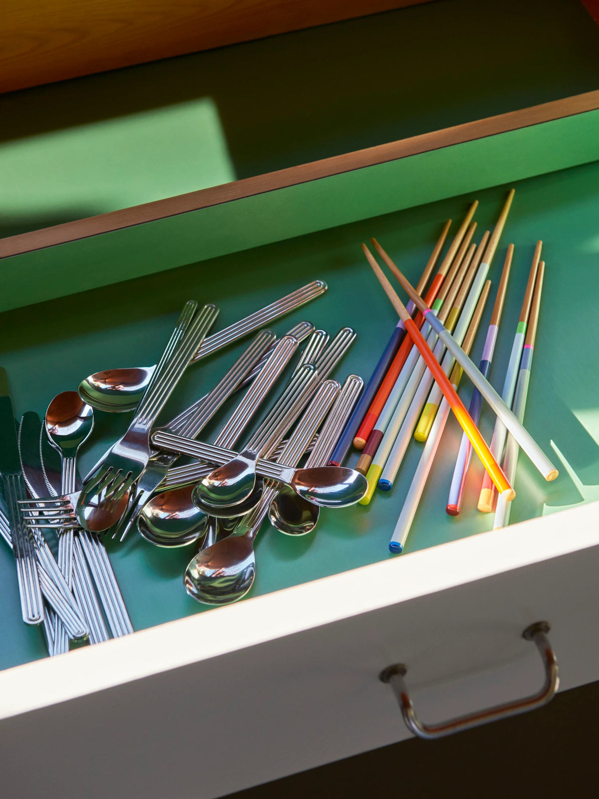 Open drawer with silverware and colorful HAY Colour Sticks Chopsticks on a green surface