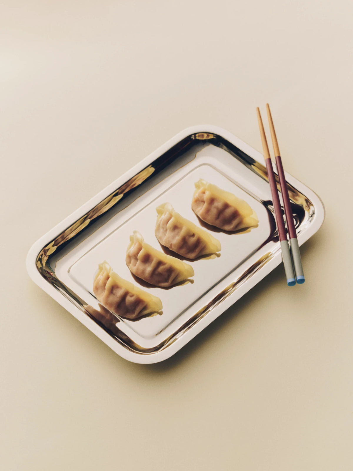 Four dumplings on a decorative tray with HAY Colour Sticks Chopsticks on a beige background
