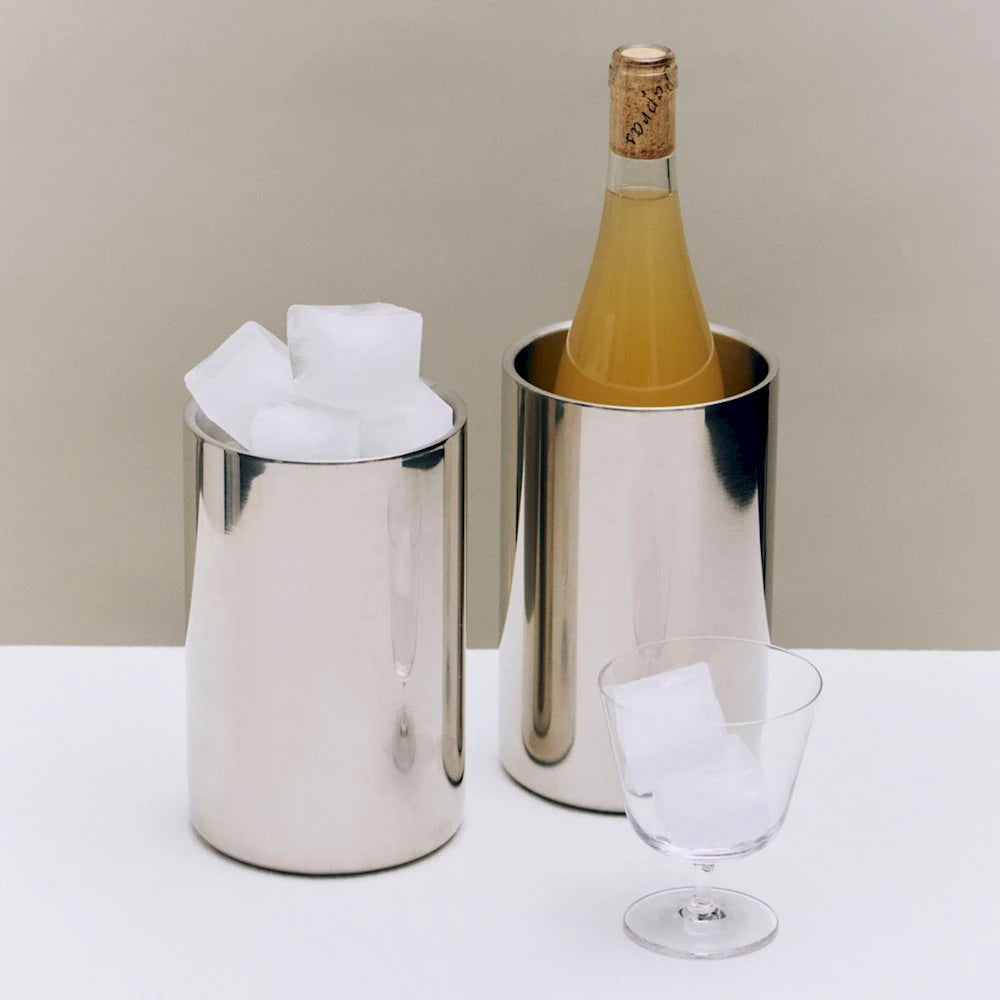 2 HAY Essential Steel Wine Coolers on a white table, one filled with ice cubes and other with a corked bottle, next to a glass