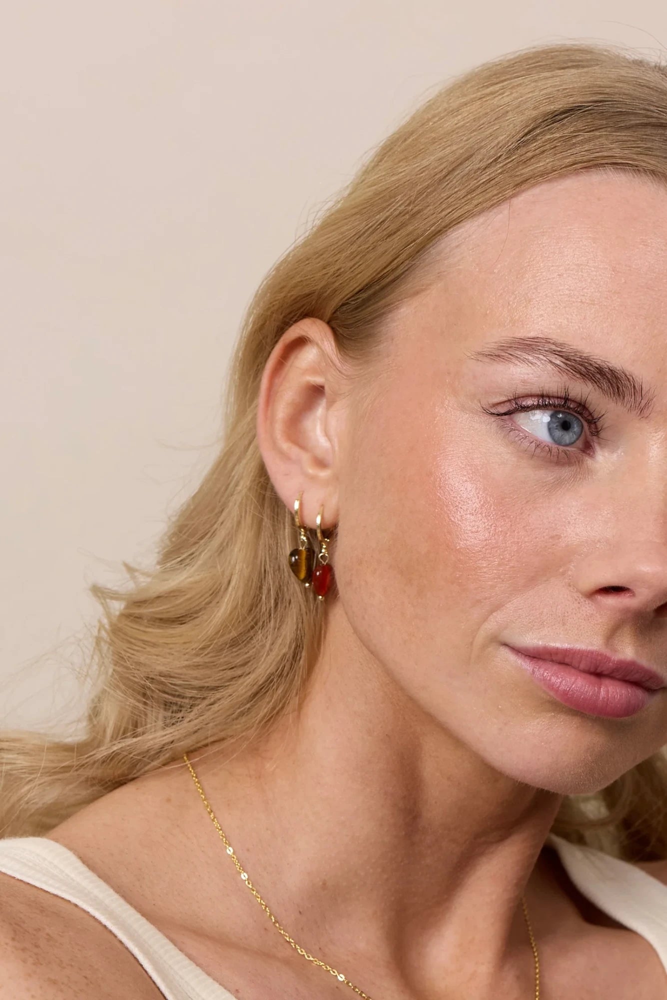 Woman wearing Soï Copenhagen Alma Tiger Eye heart earrings in 18k gold