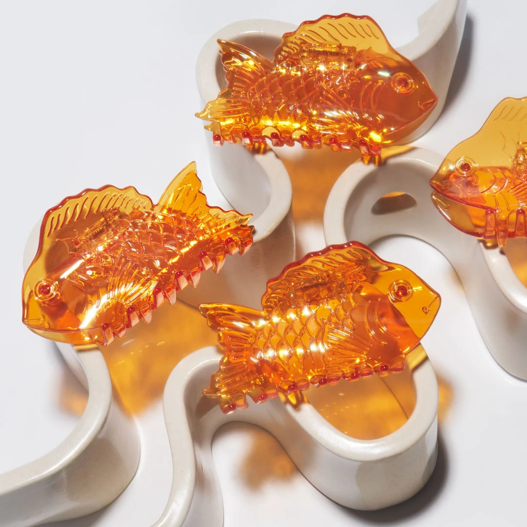 A group of Winona Irene Sea Bream Ocean Fish Acetate Hair Claws in clear orange on a white wavey ceramic dish