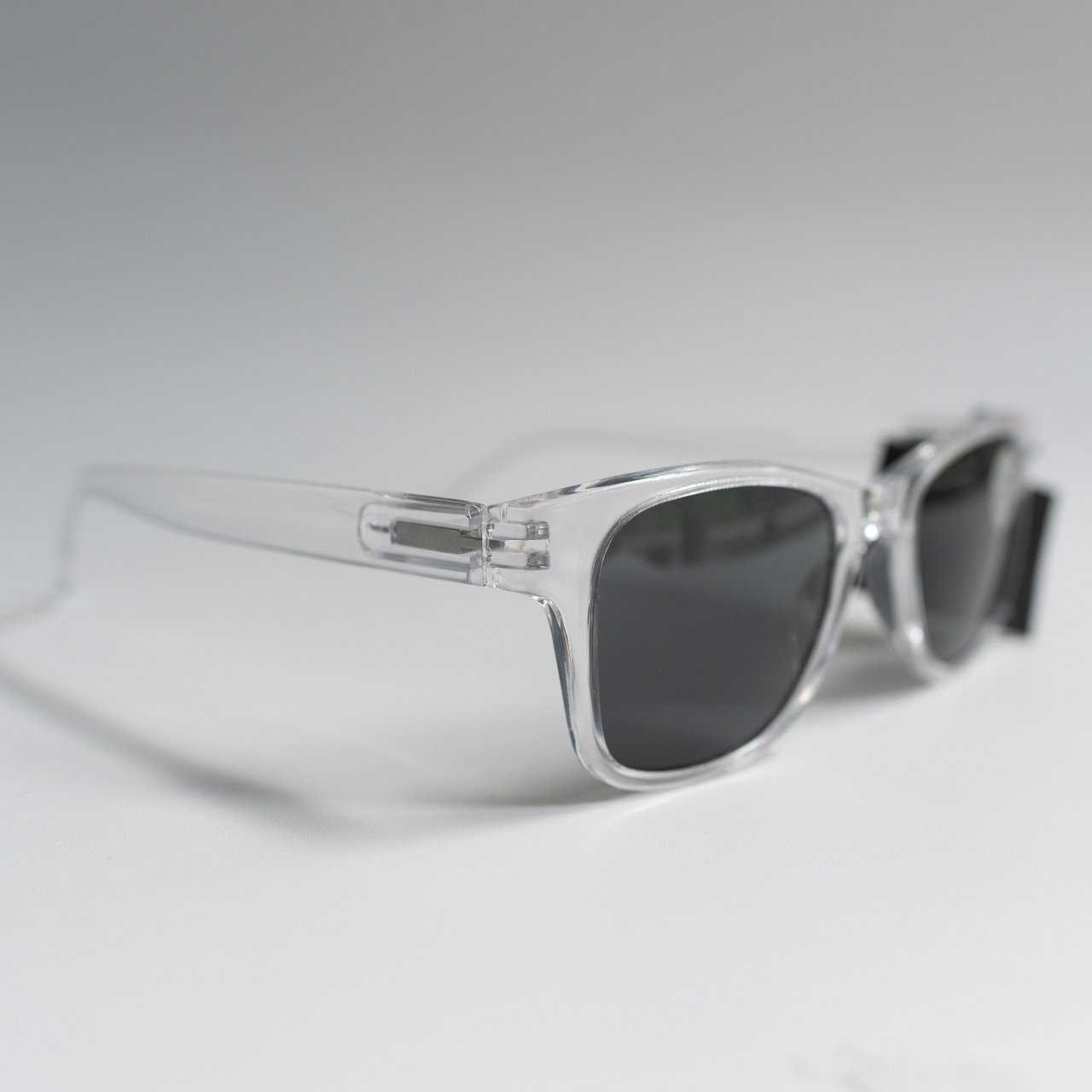 Clear frame sunglasses with dark lenses on a light gray background