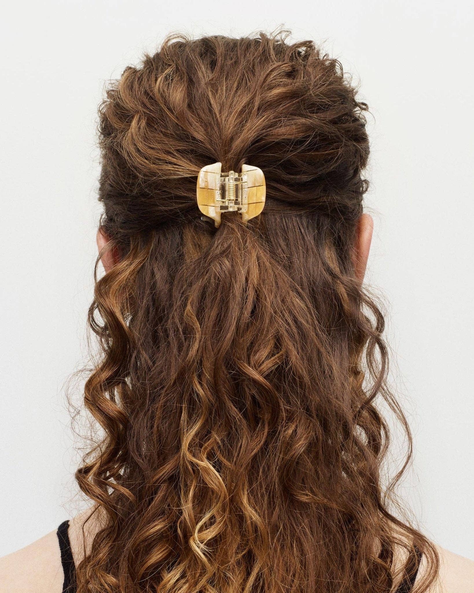 The back view of a white female model with long curly brown hair wearing the MACHETE mini hair claw to create a half up hair style