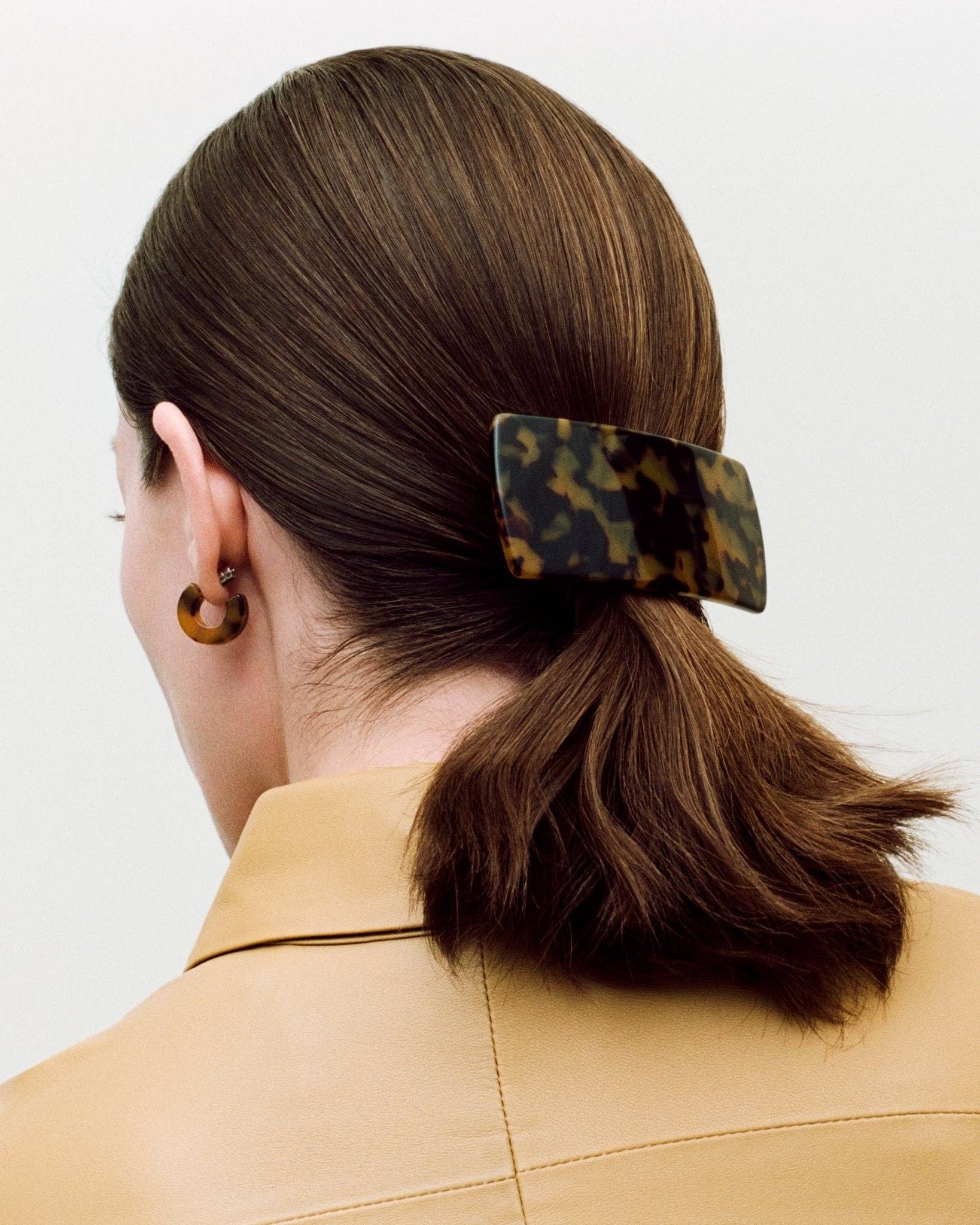 The view of the left back side of a white female model with brown hair wearing the MACHETE Muse Hoops in tortoiseshell with matching hair barrett