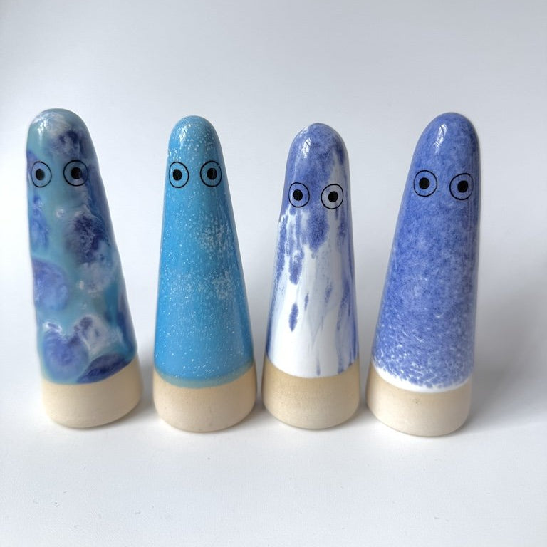 Four Studio Arhoj ghosts in shades of blue, purple, and white, each with a natural wood base and large cartoon eyes, arranged in a row on a white background.