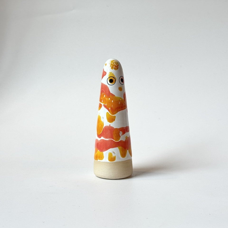 Princess Studio Arhoj ghost in orange, yellow, and white on a beige base, standing on a white surface against a light grey background.