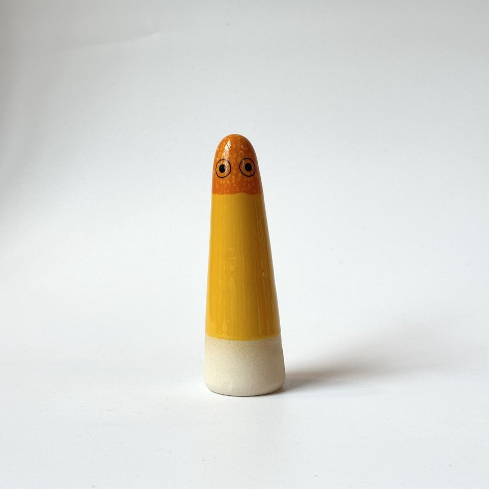 Layla Studio Arhoj ghost in orange and yellow glaze on a beige base, standing on a white surface against a light grey background.