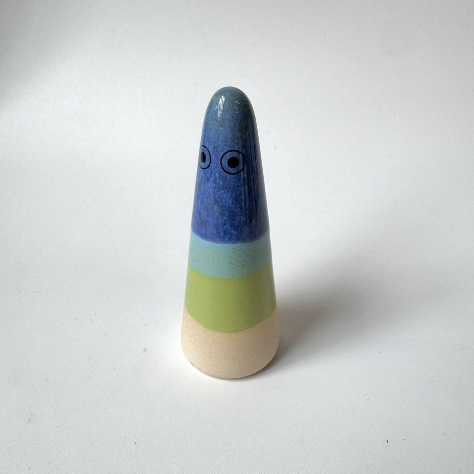 Wilfred Studio Arhoj ghost, featuring a blue top section with painted eyes, a light blue band, a pale green band, and a natural beige base, set against a plain white background.