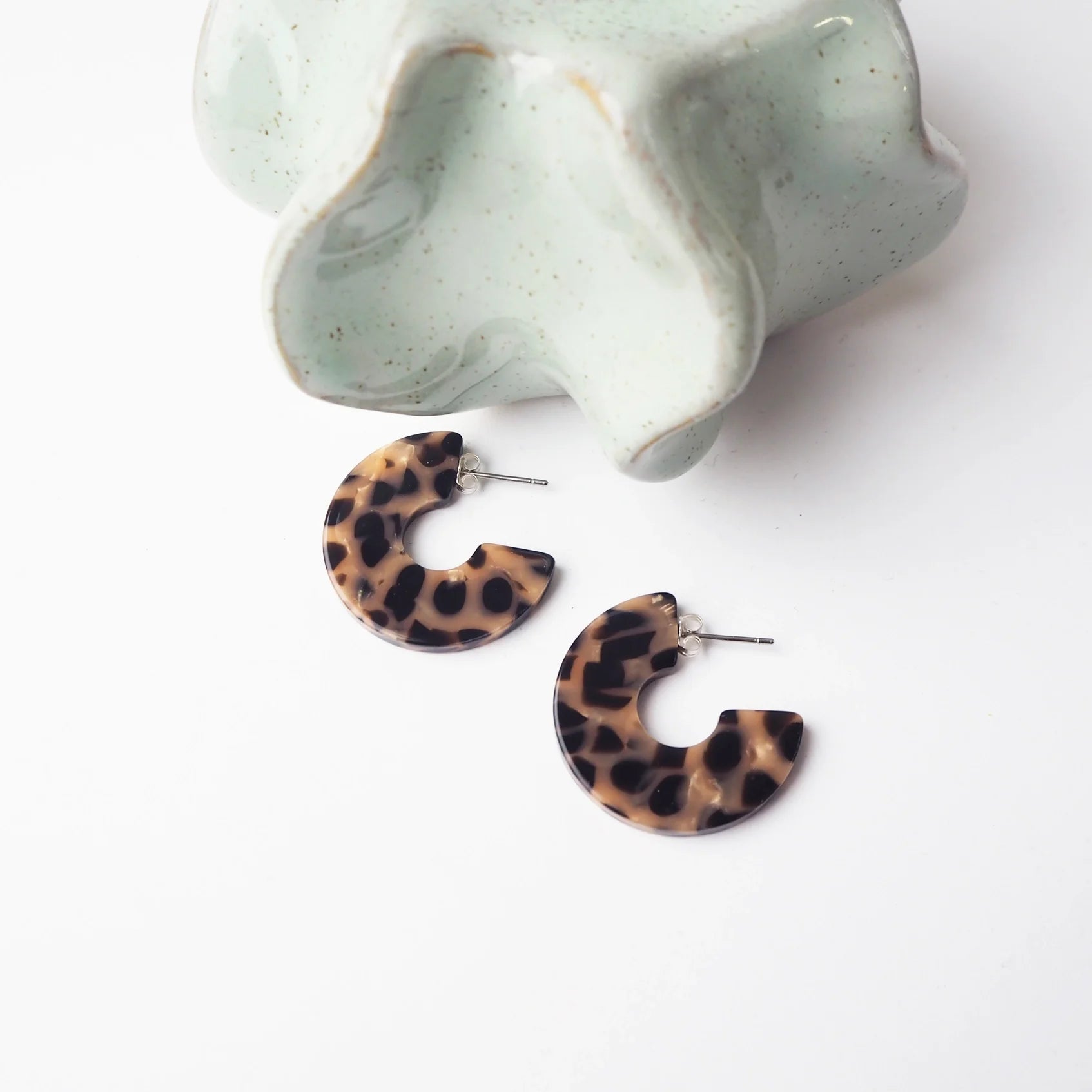 A pair of small acrylic hoop earrings in a mix of clear, blue and dark brown lying flat on a ceramic dish