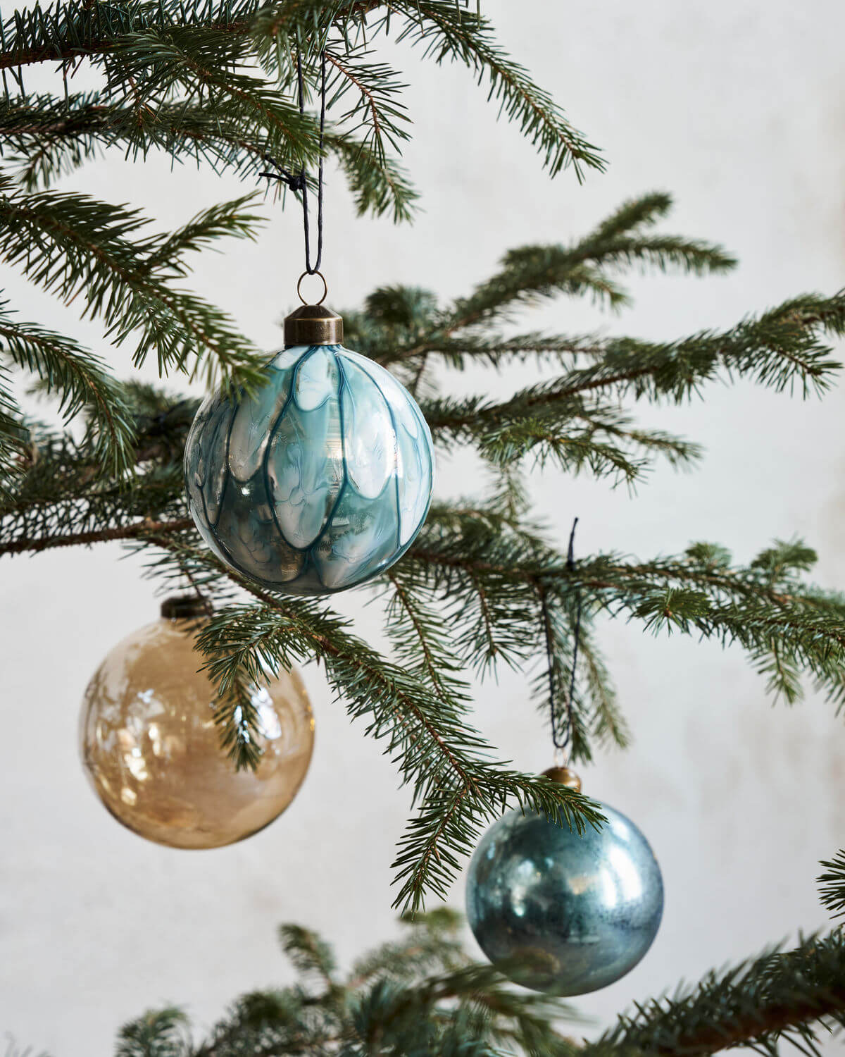 Three Christmas baubles hanging on the branch of a Christmas tree