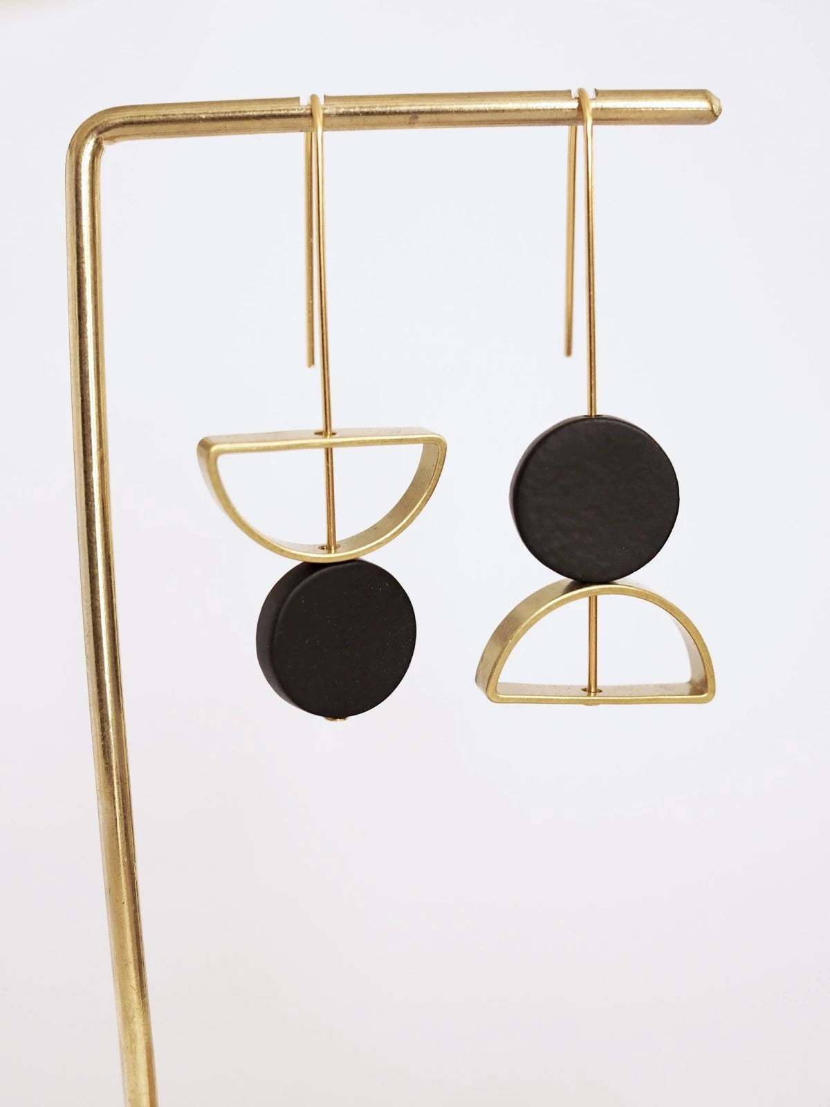 Nucleo Brass and Black Upside Down Arch Earrings by brass+bold, displayed on a gold stand against a white background.