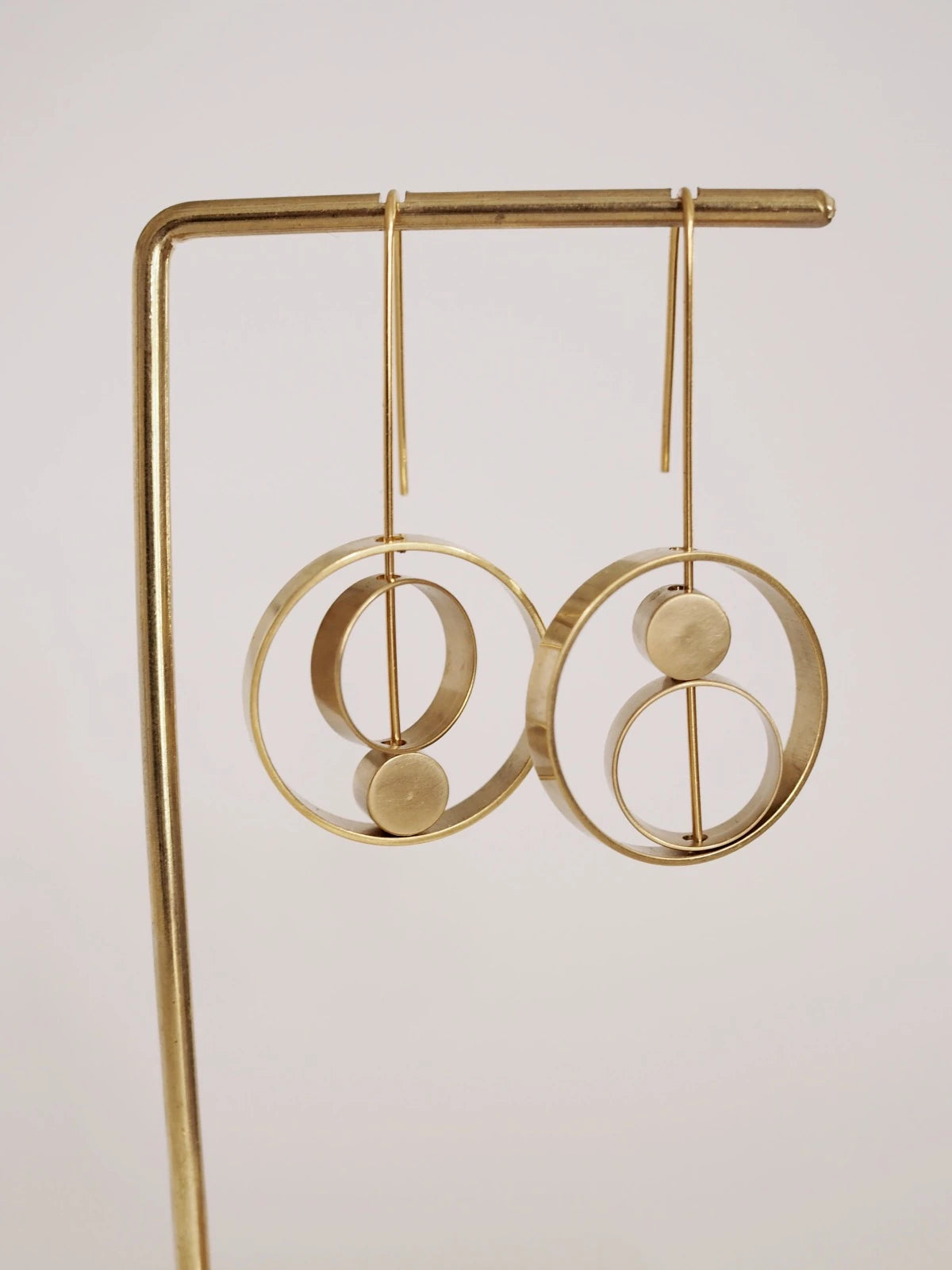 Nucleo Brass Rings within Rings Earrings by brass+bold displayed on a matching gold stand against a plain light background.
