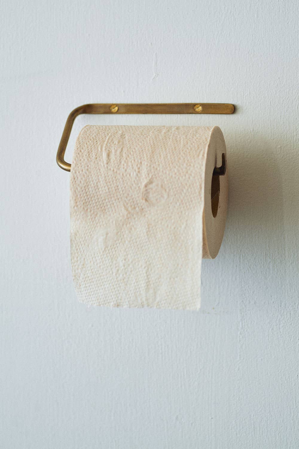 Toilet paper roll on a brass holder against a white wall