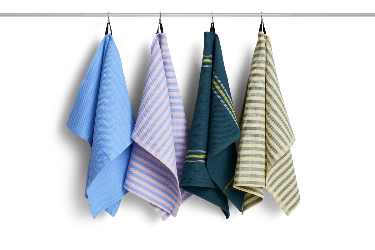 Four striped HAY Canteen kitchen towels hanging from a metal rod against a white background. The towels feature vertical stripes in light blue, lavender-pink, dark teal, and cream with olive green accents.