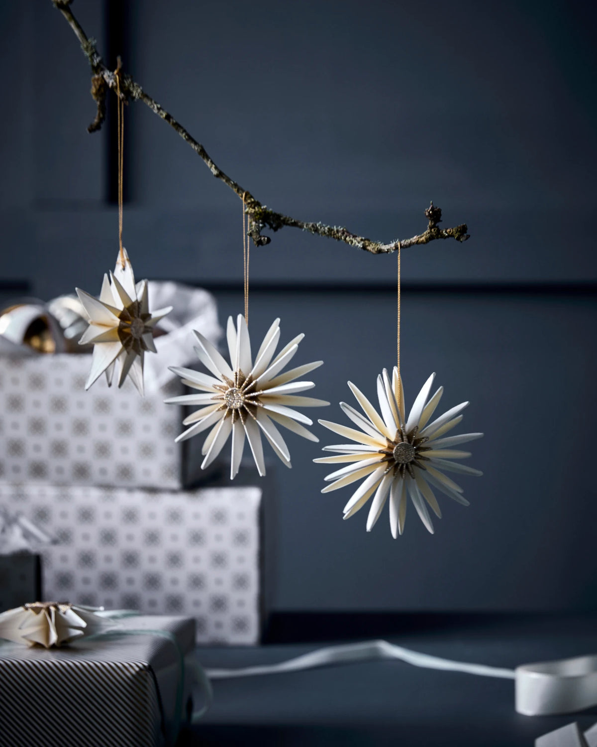 Decorative star-shaped HDStar ornaments by House Doctor, Champagne colour,  hanging from a branch against a dark background.