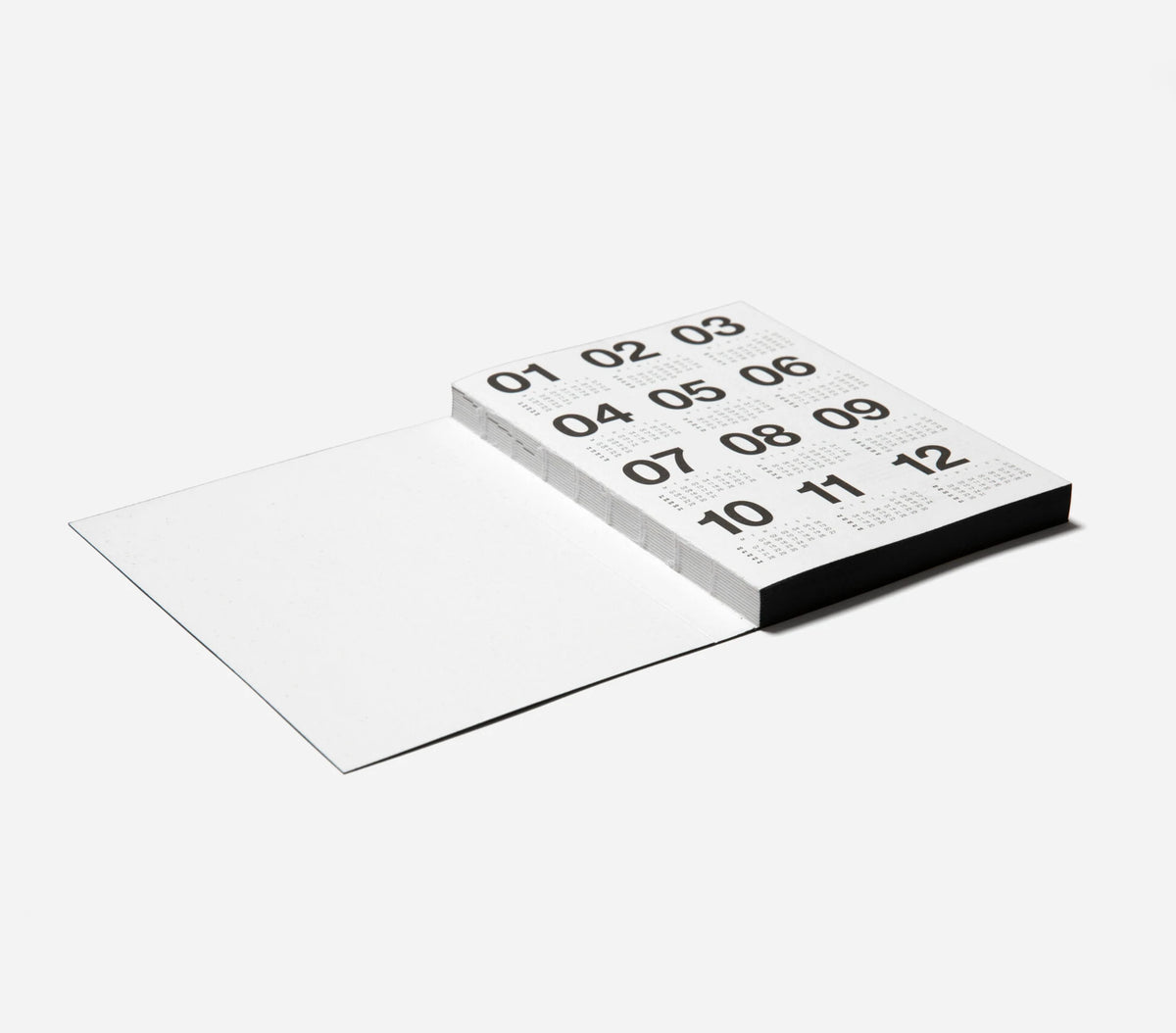 A minimalist black and white Marjolein Delhaas planner shown open, with the outer cover displaying numbers 01 through 12 in a grid pattern.