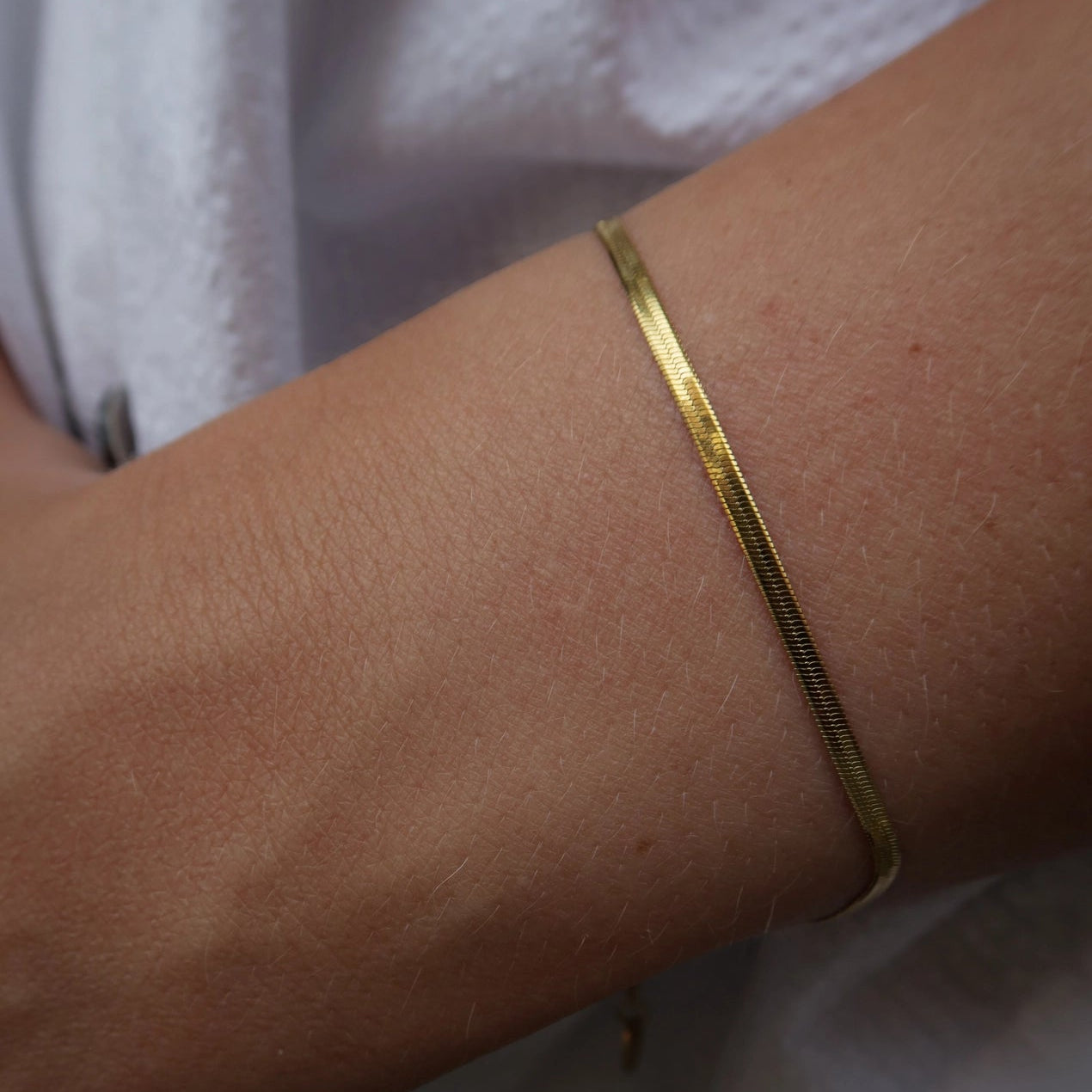 A close-up of a person's wrist wearing a thin, polished gold snake chain bracelet.