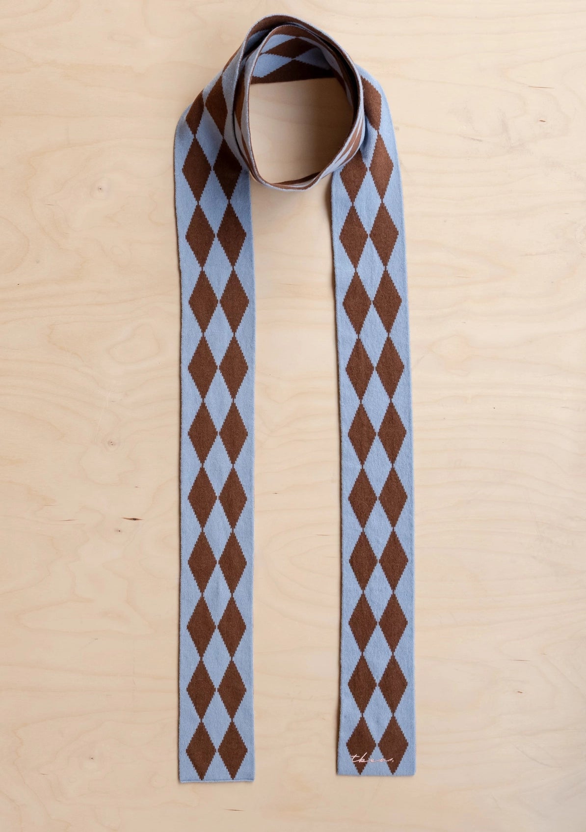 Harlequin-patterned skinny scarf with brown and blue diamonds on a beige background