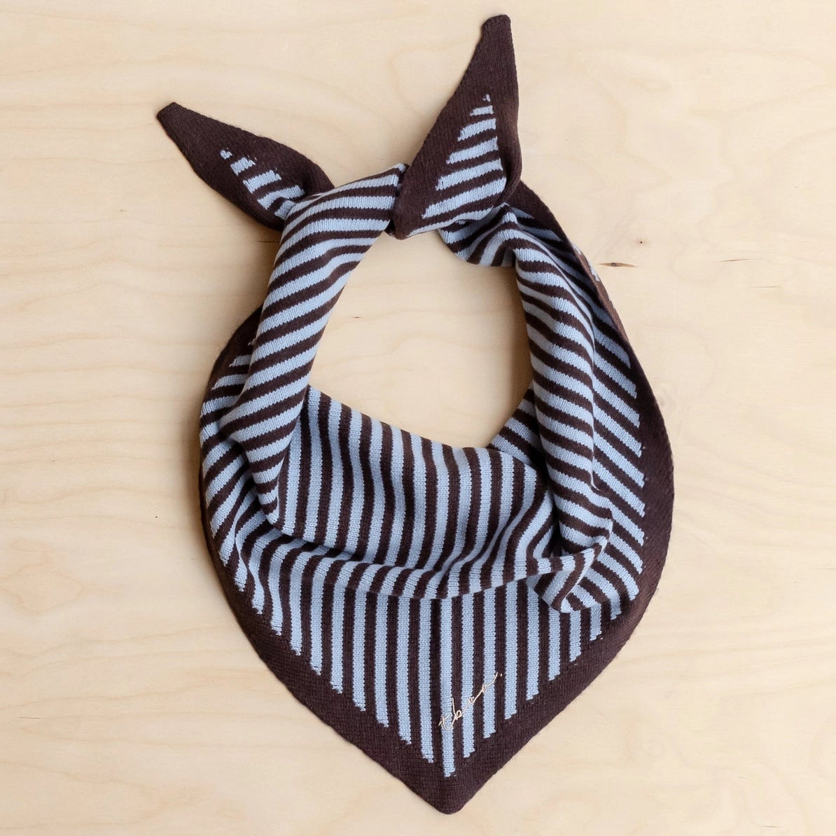 Striped TBCo triangle scarf with brown border on a beige background