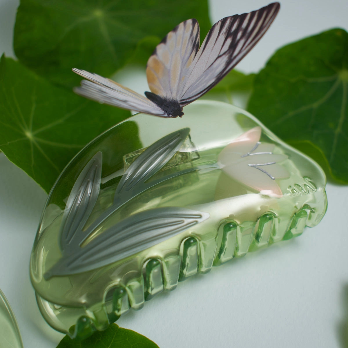 Clear green plastic clip with lotus flower and leaf design on green leaves