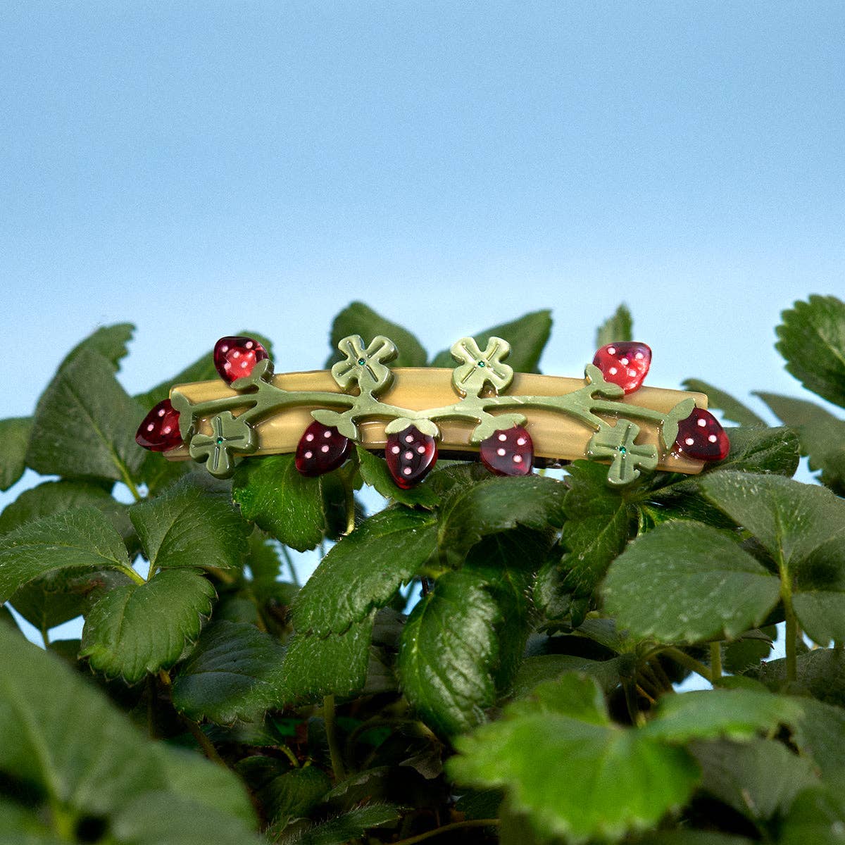 Decorative barrette clip with strawberry and clover designs on a green leafy background