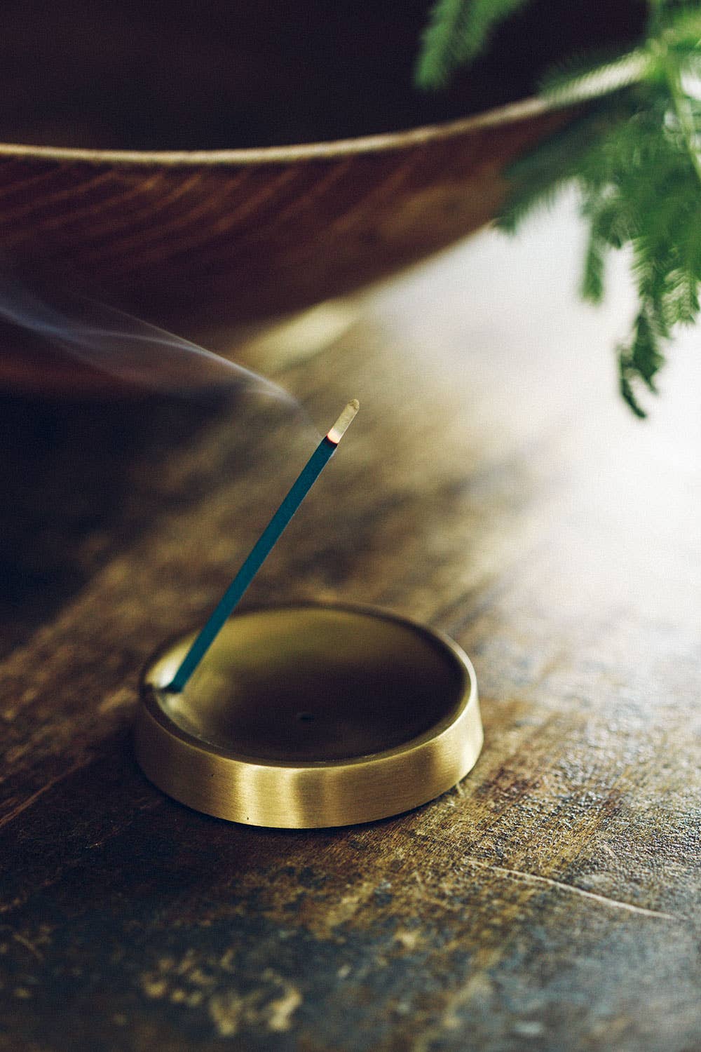 Incense stick burning in a brass holder on a wooden surface with a blurred background