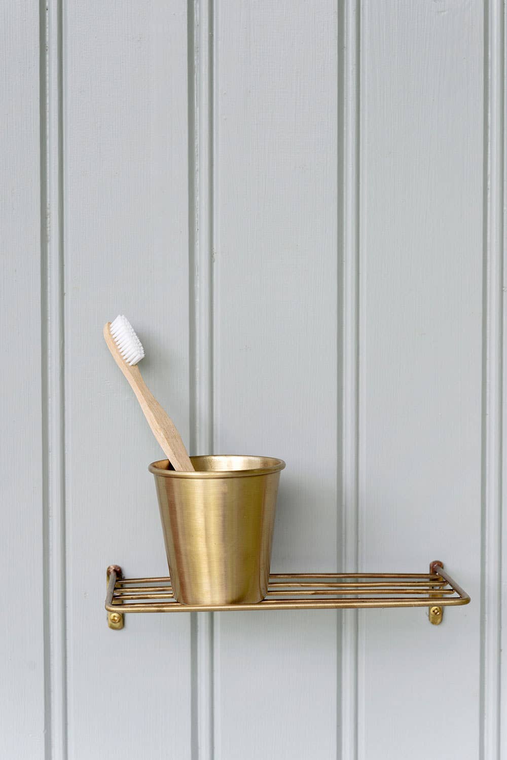 Brass cup and toothbrush on a brass shelf against a gray paneled wall