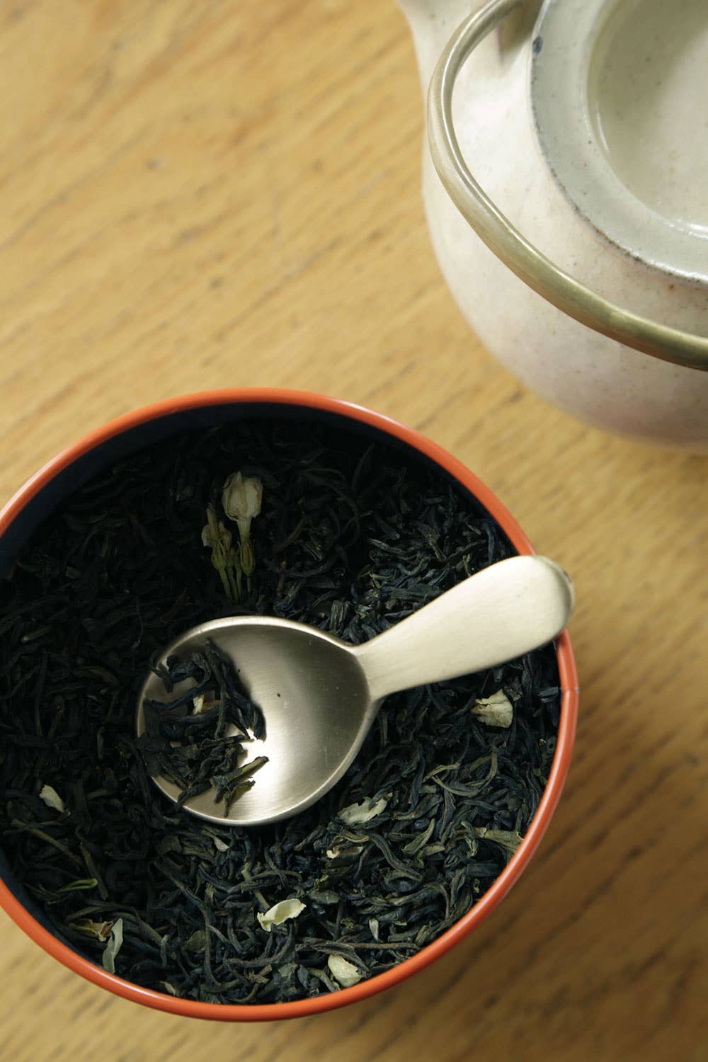 Tea leaves in a red bowl with a brass  spoon on a wooden surface