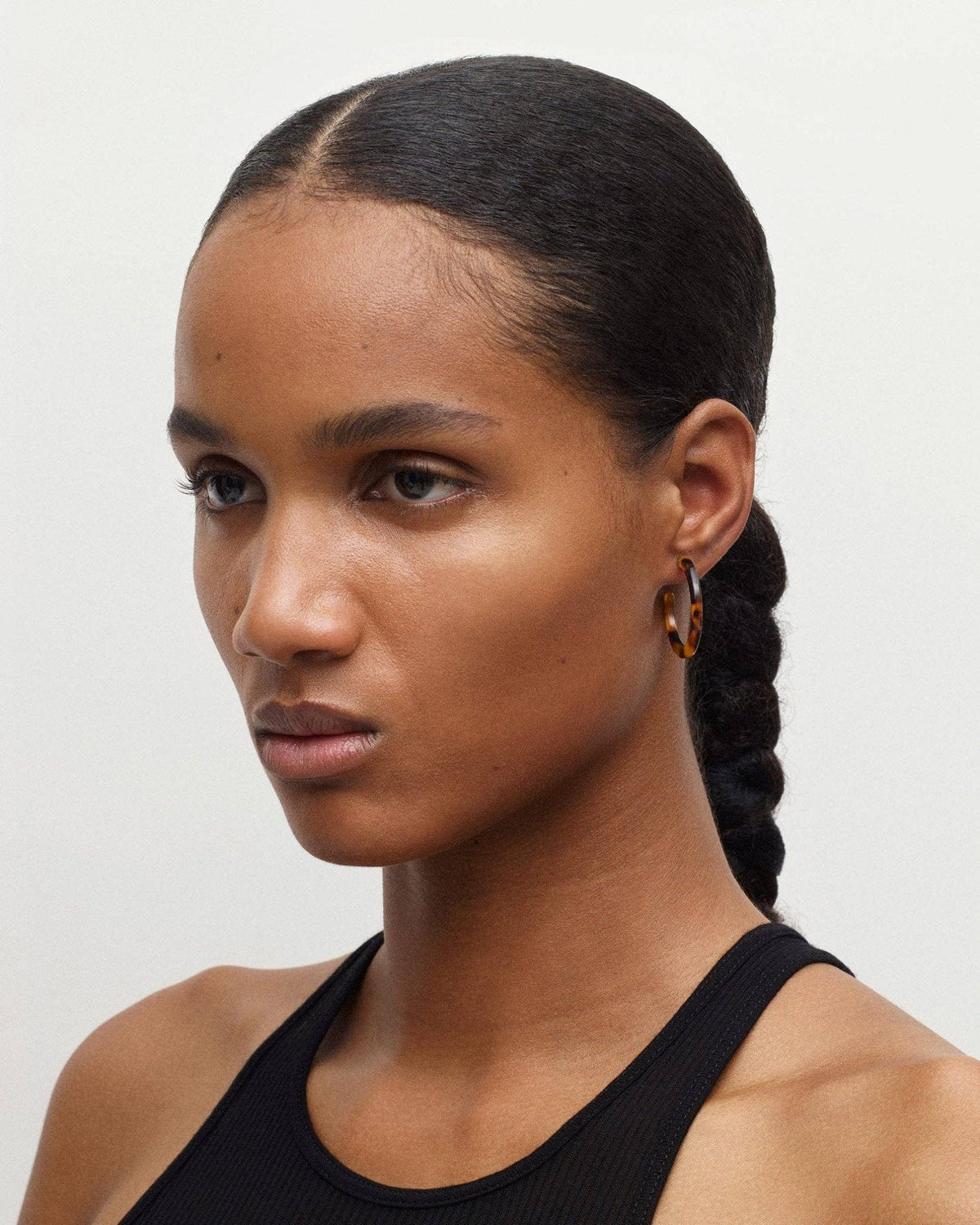 The front side angle of a model with her hair tied back wearing the MACHETE mini hoops in classic tortoise