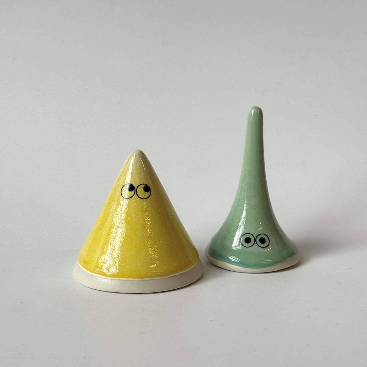 Lucy, a green Studio Arhoj familia from the Yoko family standing on a plain light grey background.