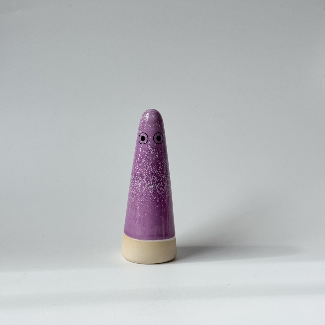 Odette Studio Arhoj ghost with a purple speckled body and a beige base, featuring simple black eyes, set against a plain light grey background.