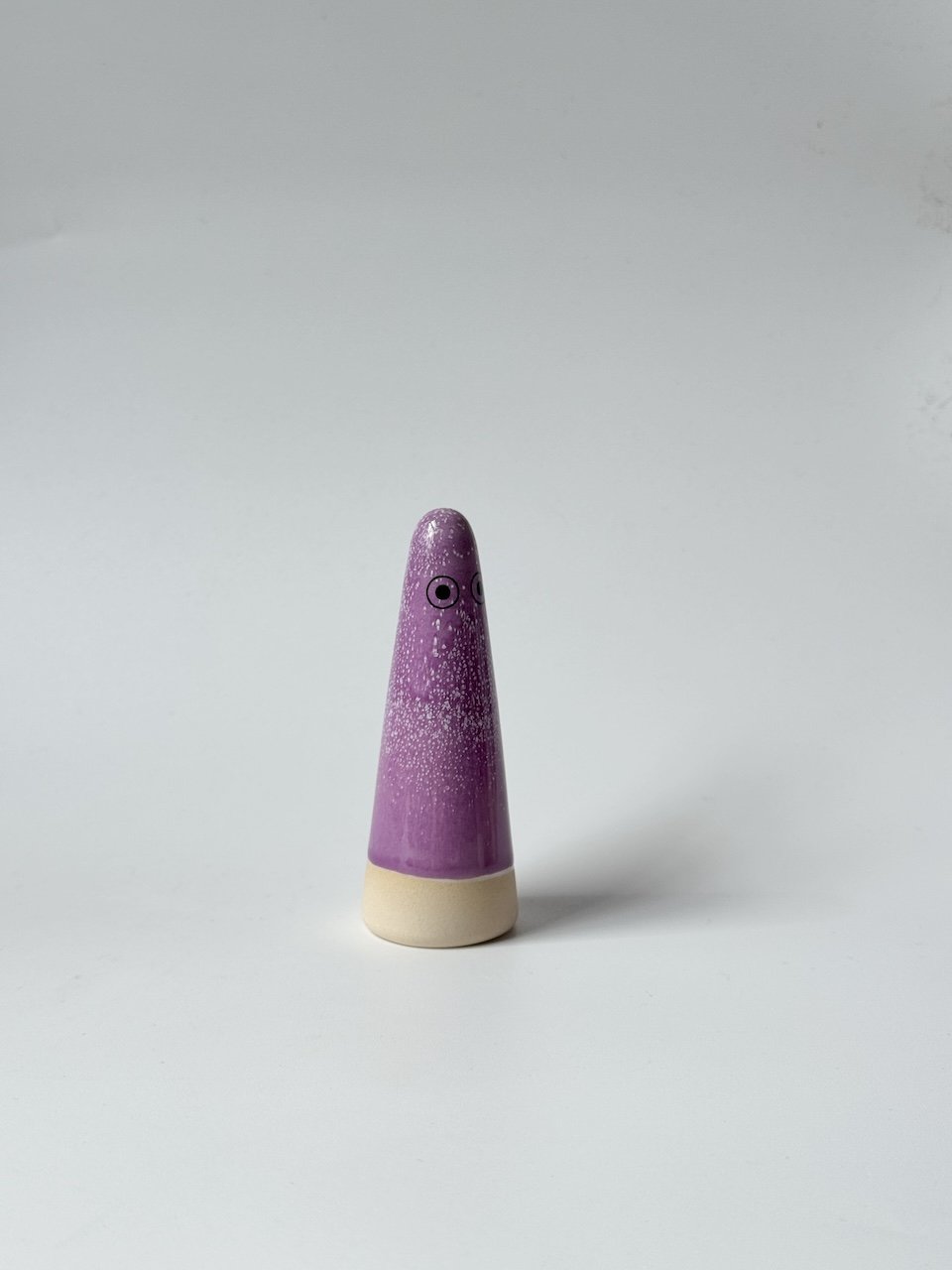 Odette Studio Arhoj ghost with a purple speckled body and a beige base, featuring simple black eyes, set against a plain light grey background.